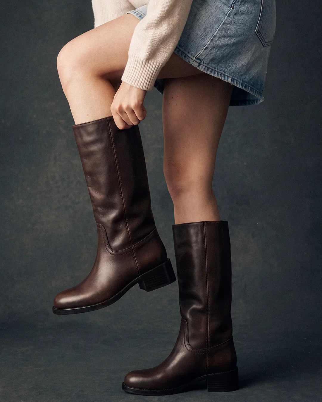 Woman checking the fit of brown knee-high boots around her calf